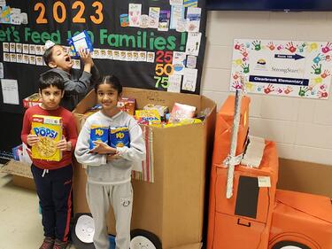 Three students stand in front of large box filled with food donations