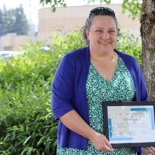 Female stands outside next to tree holding framed award