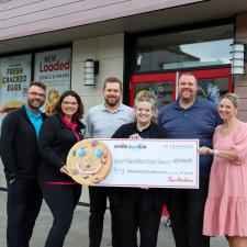 Owners of Tim Hortons and Manager of community outreach for Abbyschools stand in front of Tim Hortons holding large cheque