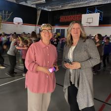 Two staff pose and smile, students in the background of the gym dancing