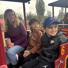 Two elementary students and an adult sit on a bench seat located on a train, waiting to go for a train ride.