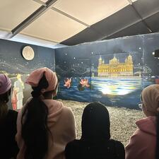 Highschool students watch a presentation together in a dark room with minimal light at their field trip to Gobind Sarvar